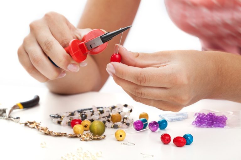 Personne assemblant des boucles d’oreilles à la main avec pinces, perles et crochets sur une table d’atelier