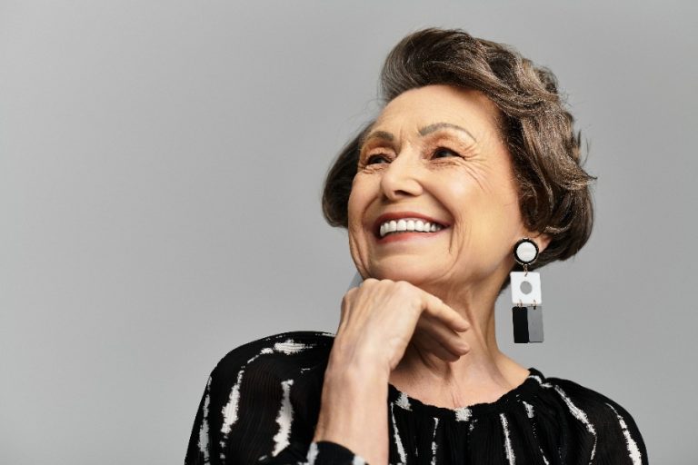 Femme élégante de 60 ans portant des boucles d’oreilles en or, mettant en valeur son port de tête et son sourire