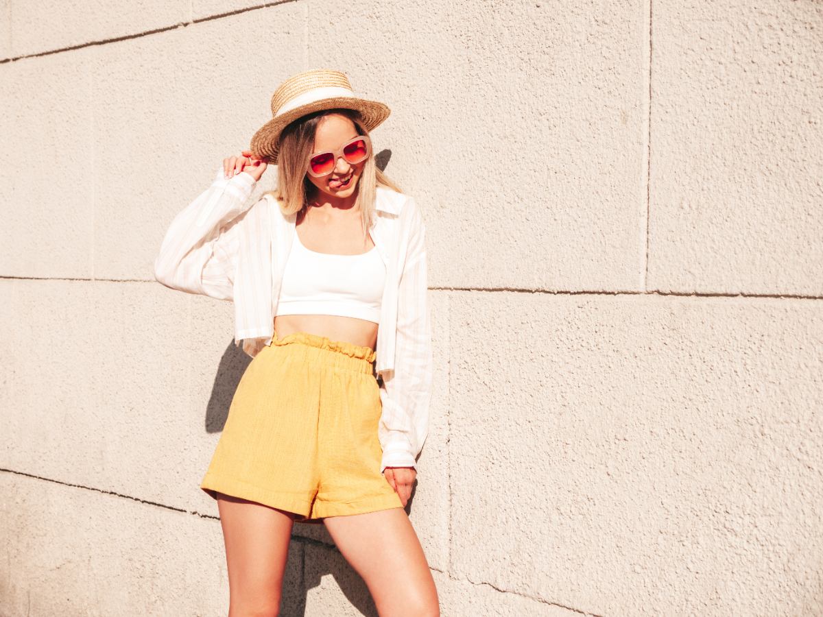 Une femme portant un short taille haute jaune avec un haut blanc et un chapeau