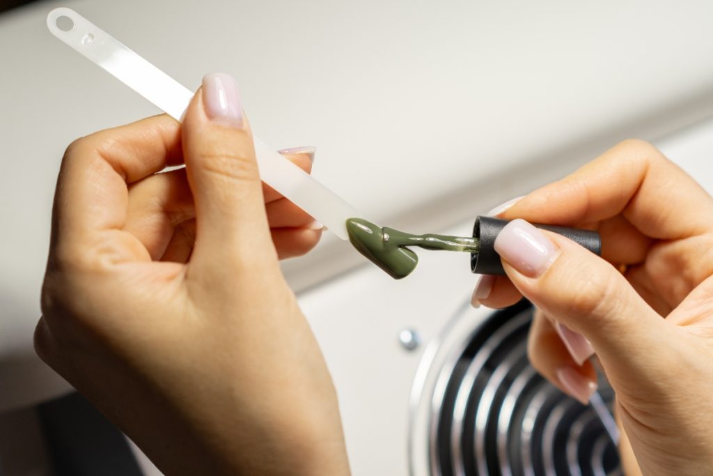 Une femme qui applique du vernis à ongles vert kaki sur du faux ongle