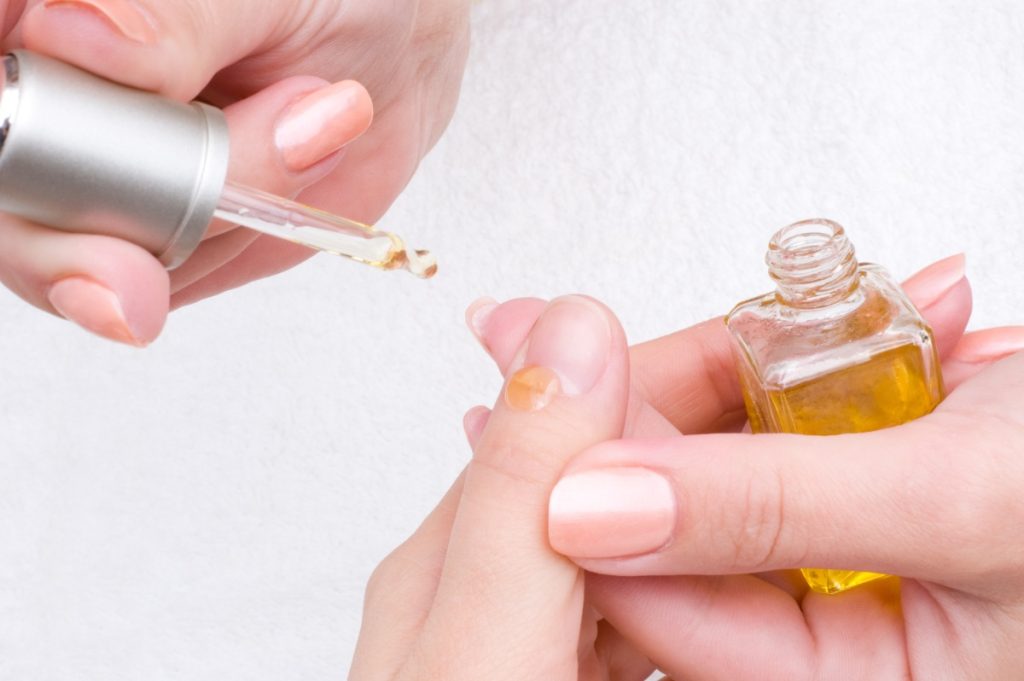 Mains appliquant de l'huile de ricin sur ses ongles