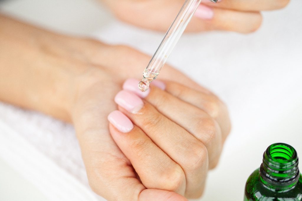 Main d'une femme qui applique de l'huile de ricin sur les cuticules