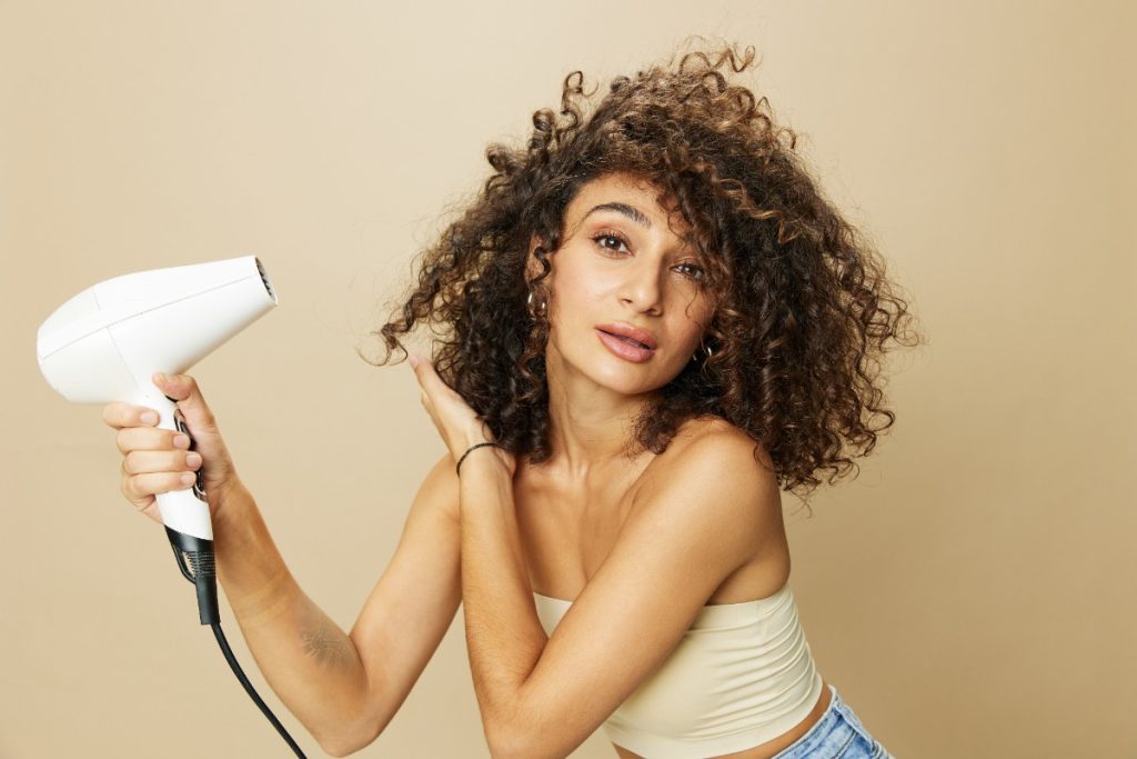 Une femme aux cheveux bouclés utilisant un sèche-cheveux
