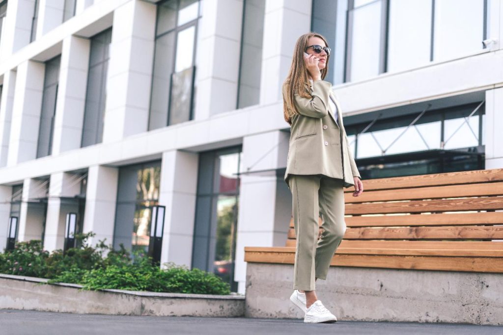 Une femme au téléphone portant un tailleur beige et un basket blanc