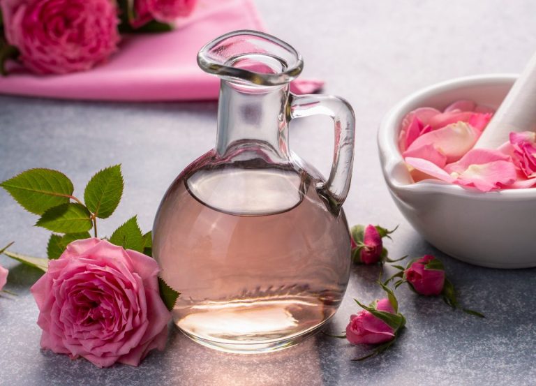 Eau de rose dans un pichet en verre avec des fleurs sur la table