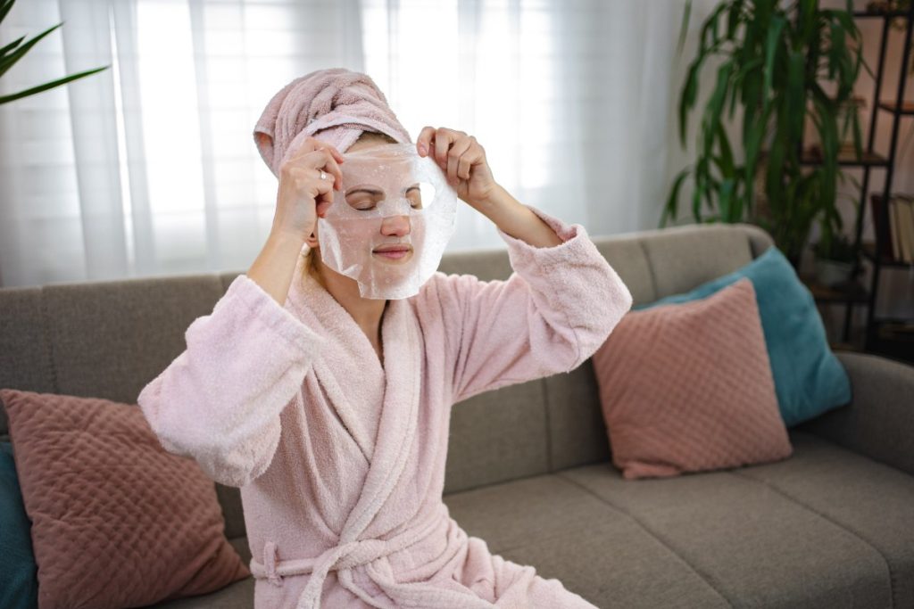 Une femme assise sur un canapé et appliquant un masque facial