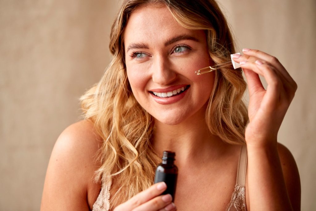 Une femme souriante appliquant du sérum sur le visage