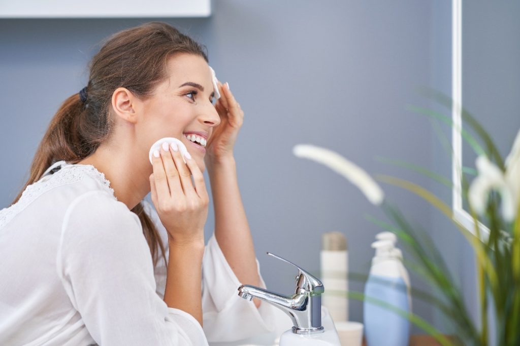 Une femme souriante nettoyant son visage dans la salle de bain