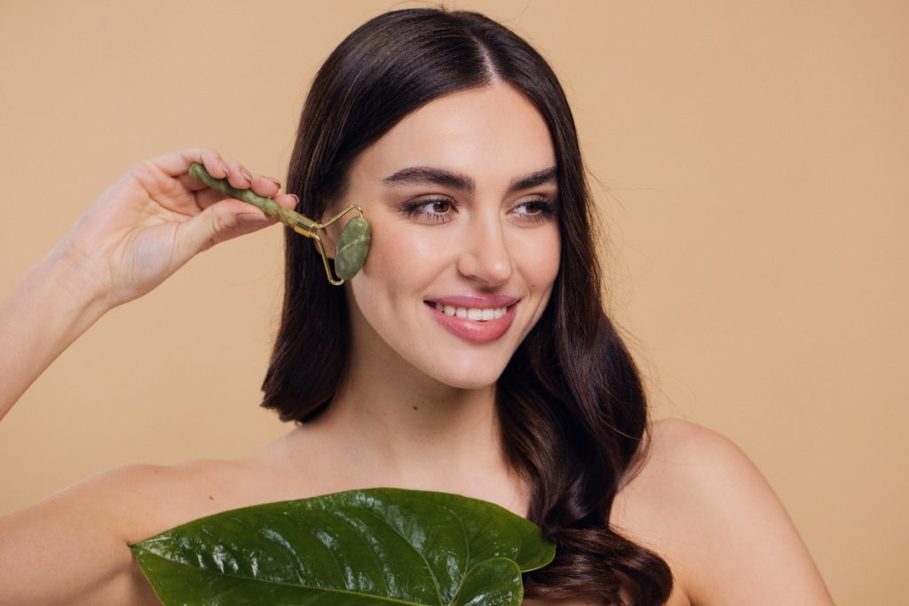 Une femme souriante utilisant un rouleau de jade sur le visage