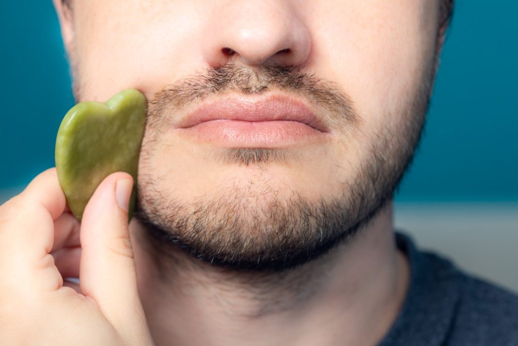 Un homme utilisant du gua sha sur son visage